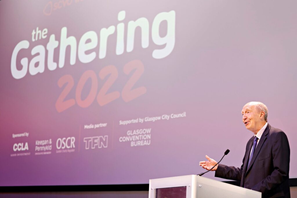 SCVO convener, Andrew Burns, speaks at a lectern in front of a large sign that says "the Gathering 2022"