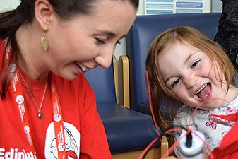 A woman and a child are shown. They are both smiling and happy. There are wires on the screen, suggesting a medical setting.