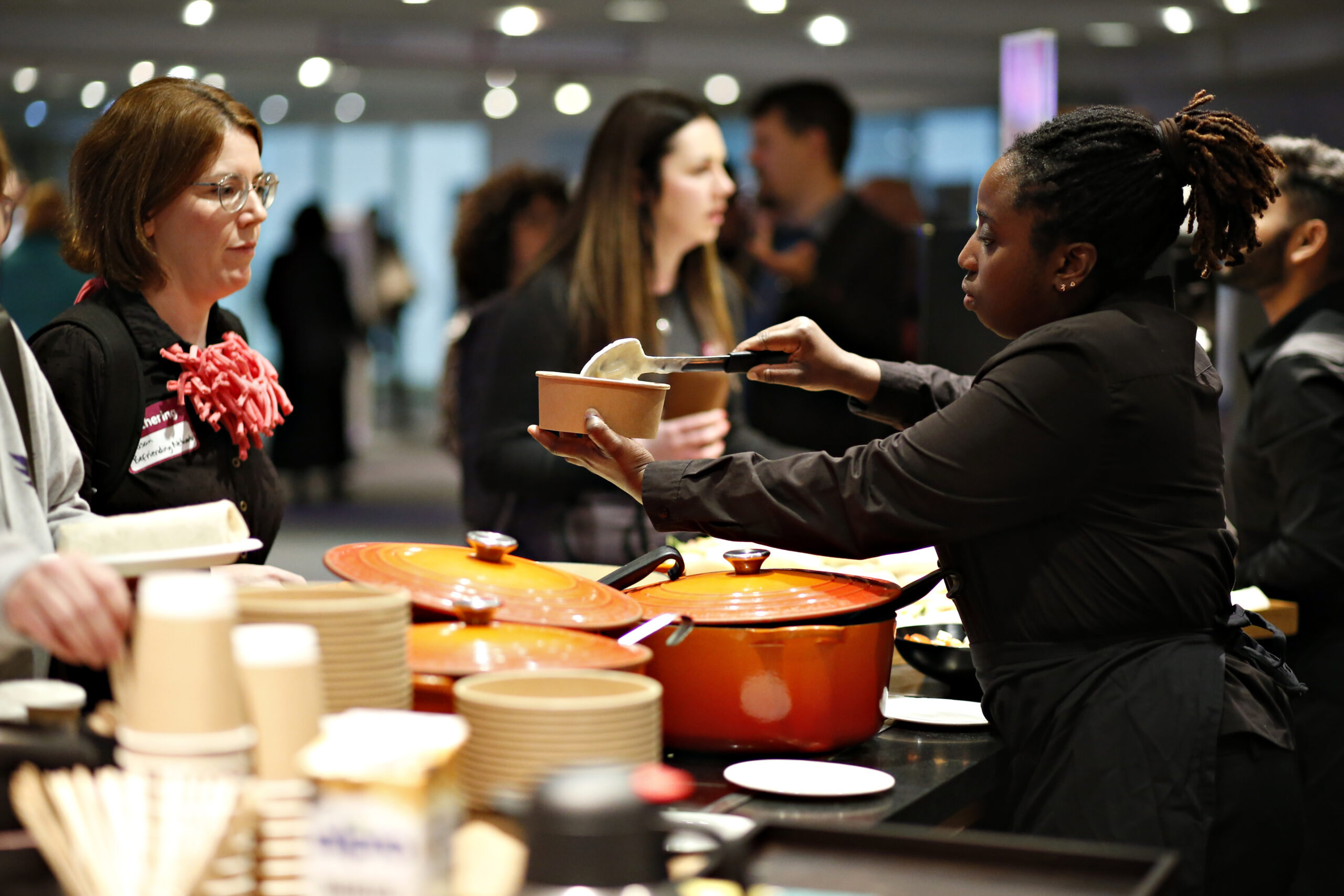 Catering stall at the Gathering. A woman serves a delegate food from an orange dish