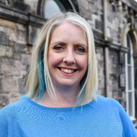 Headshot photo of Gail Burden - a woman wearing a blue top with long blonde hair with blue highlights smiling