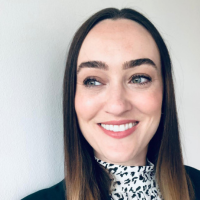 Headshot photo of Zoe Greenfield- a woman wearing a black and white patterned turtle-necked top with long brown hair smiling