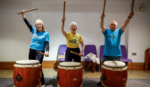 Three Taiko drummers pose with their drums and beaters.