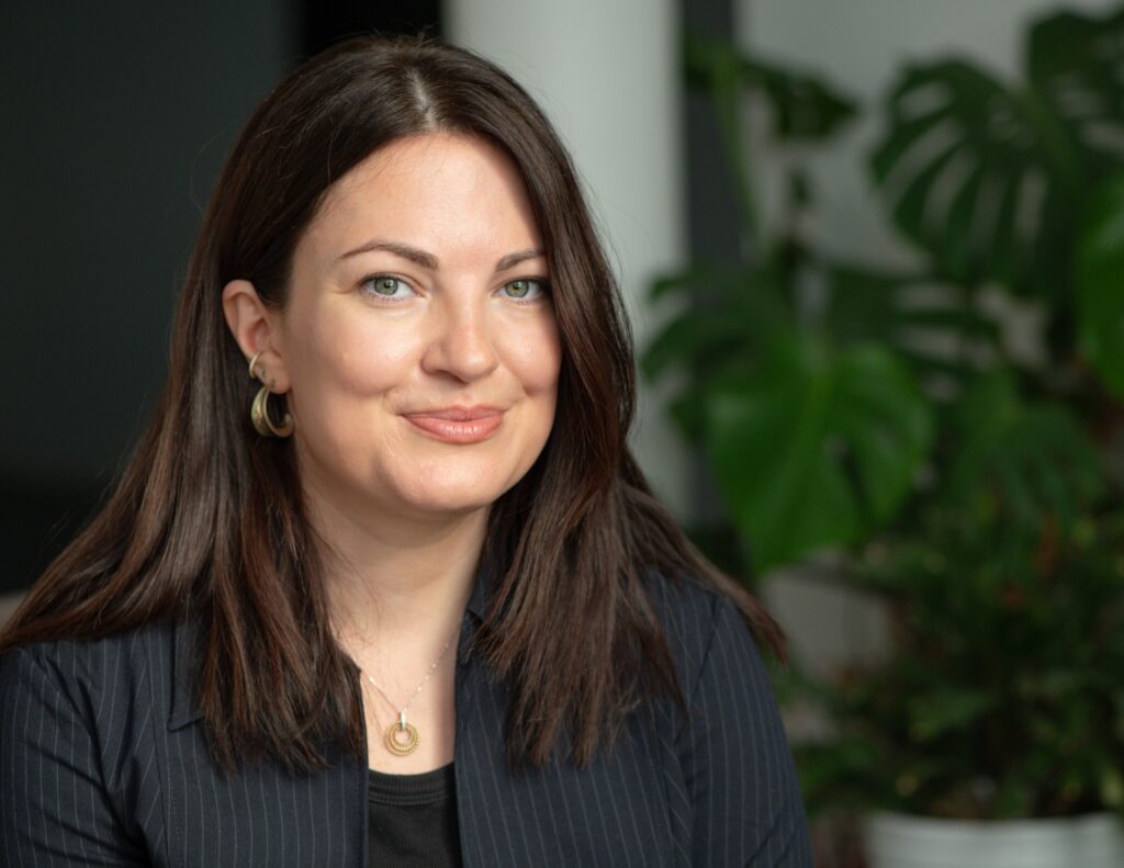 A headshot photo of Jane Mackinnon, a white woman with dark straight hair and blue eyes.