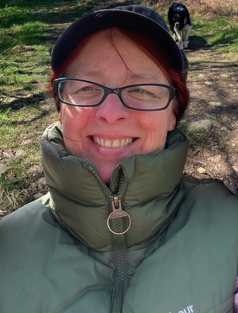 Headshot of Becca Nelson, a white woman with dark hair, wearing glasses and a baseball cap.