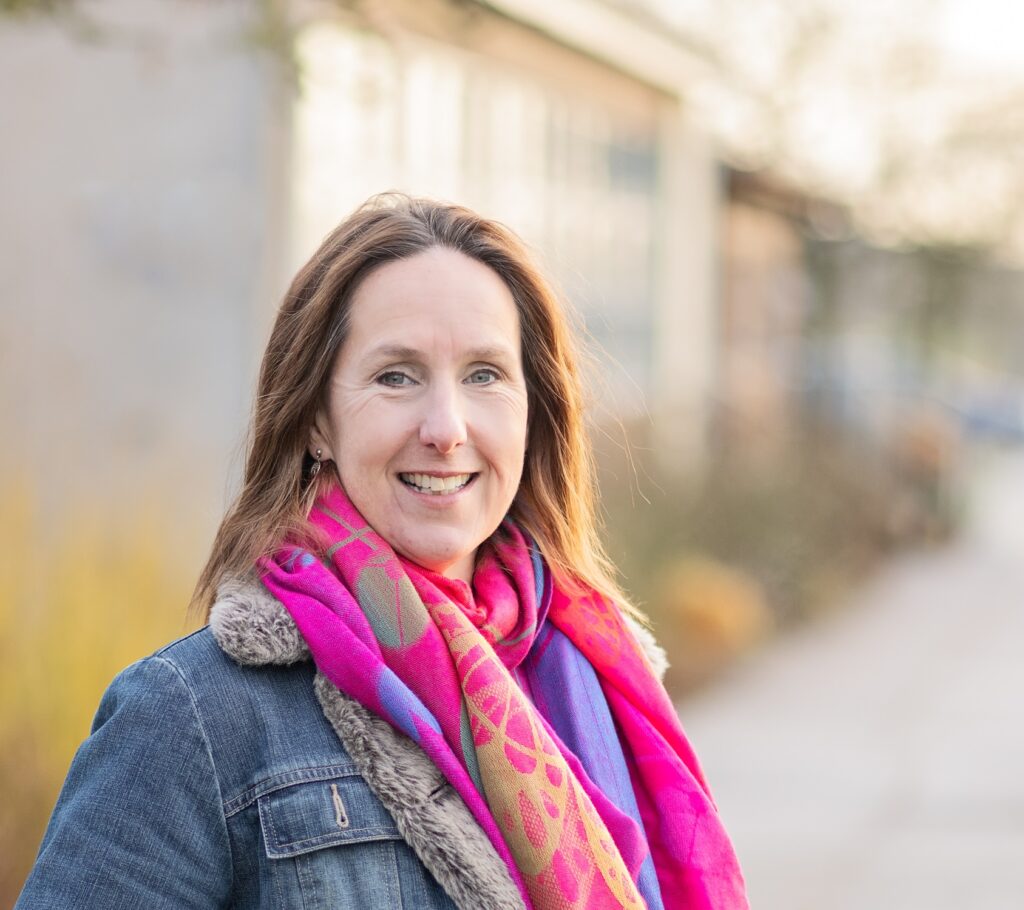 Headshot of Danielle Dale, a woman with mid-length brown hair wearing a pink scarf.