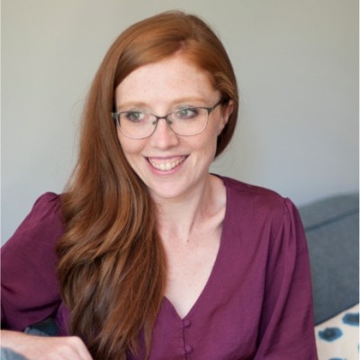 Headshot of Kim Holmes, a white woman with red hair and glasses.